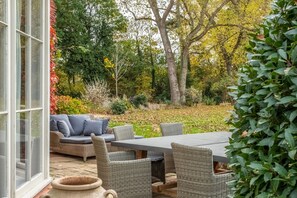 An outdoor patio with wicker furniture, a table, and a glass door leading to a garden. - Holmbush, Thornham, Norfolk (Thornham)