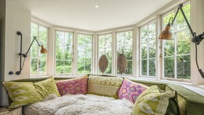 A bay window with multiple panes, a plush green sofa with patterned cushions, and two wall-mounted lamps. - Holmbush, Thornham, Norfolk (Thornham)