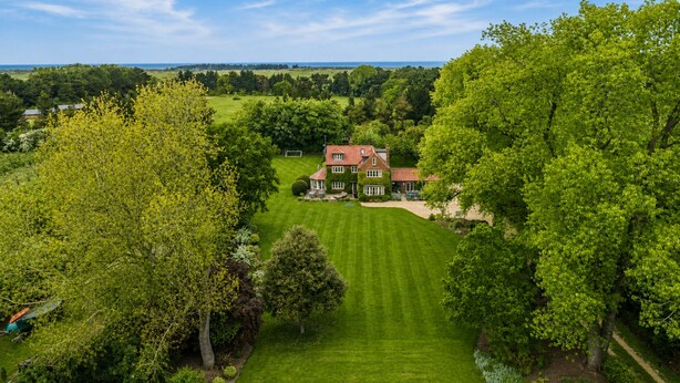 A large house with a well-manicured lawn, surrounded by trees and a clear sky. - Holmbush, Thornham, Norfolk (Thornham)