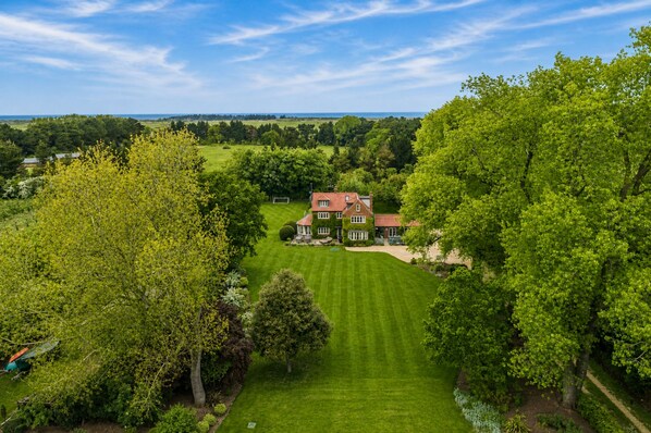 A large house with a well-manicured lawn, surrounded by trees and a clear sky.