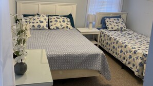 A bedroom with two beds, a ceiling fan, a nightstand, a lamp, and a framed picture on the wall. - Beach Block Beauty with Ocean Views (Wildwood)