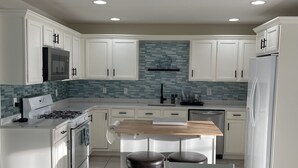 A modern kitchen with white cabinets, a wooden island, and a tiled backsplash. - Beach Block Beauty with Ocean Views (Wildwood)