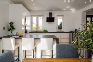 A modern kitchen with a central island, white cabinetry, and a flat-screen TV mounted above the island.