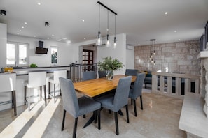 A modern kitchen with a wooden dining table, grey upholstered chairs, and pendant lighting.
