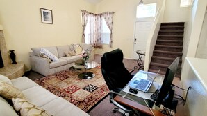 A living room with a sofa, a coffee table, a black office chair, and a laptop on a desk. There is a staircase in the background. - 3BR 2.5 baths in this Quiet and Safe Community NW of Tucson Arizona. (Tucson)