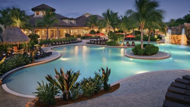 Ein Poolbereich eines Resorts mit großem Pool, Liegestühlen, Palmen und einem Wasserfall.