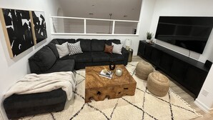 Ein modernes Wohnzimmer mit einem schwarzen Ecksofa, einem Holztisch und einem großen Flachbildfernseher.