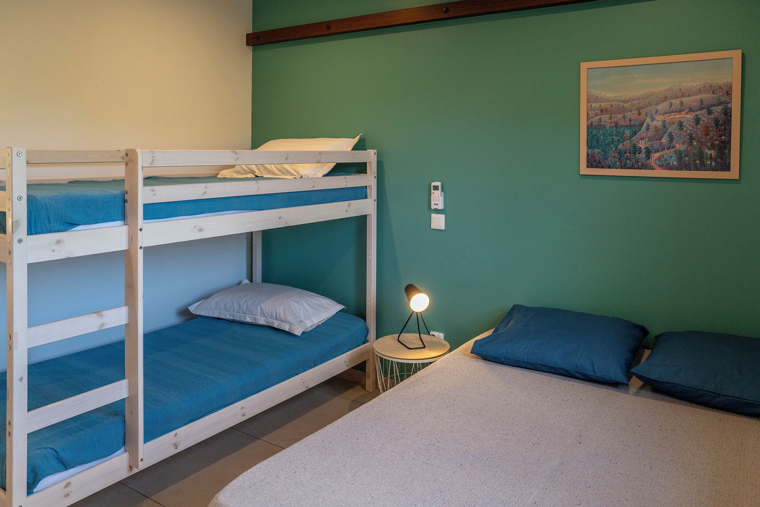 Een slaapkamer met een stapelbed, een klein tafeltje en een lamp, een schilderij aan de muur, en een groene wand.