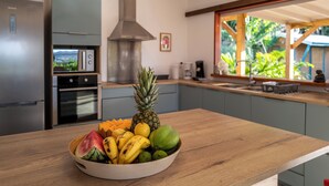 Una cocina con encimera de madera, un bol de fruta, una campana extractora de acero inoxidable y una ventana con vistas al verdor.