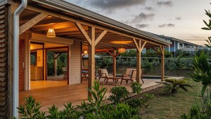 Un espacio al aire libre techado con suelo de madera y asientos, rodeado de follaje.