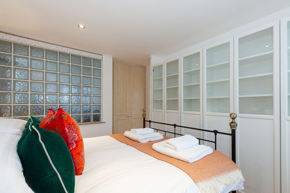 A neatly made bed with white linens and a folded towel, a window with frosted glass, and a wooden wardrobe.