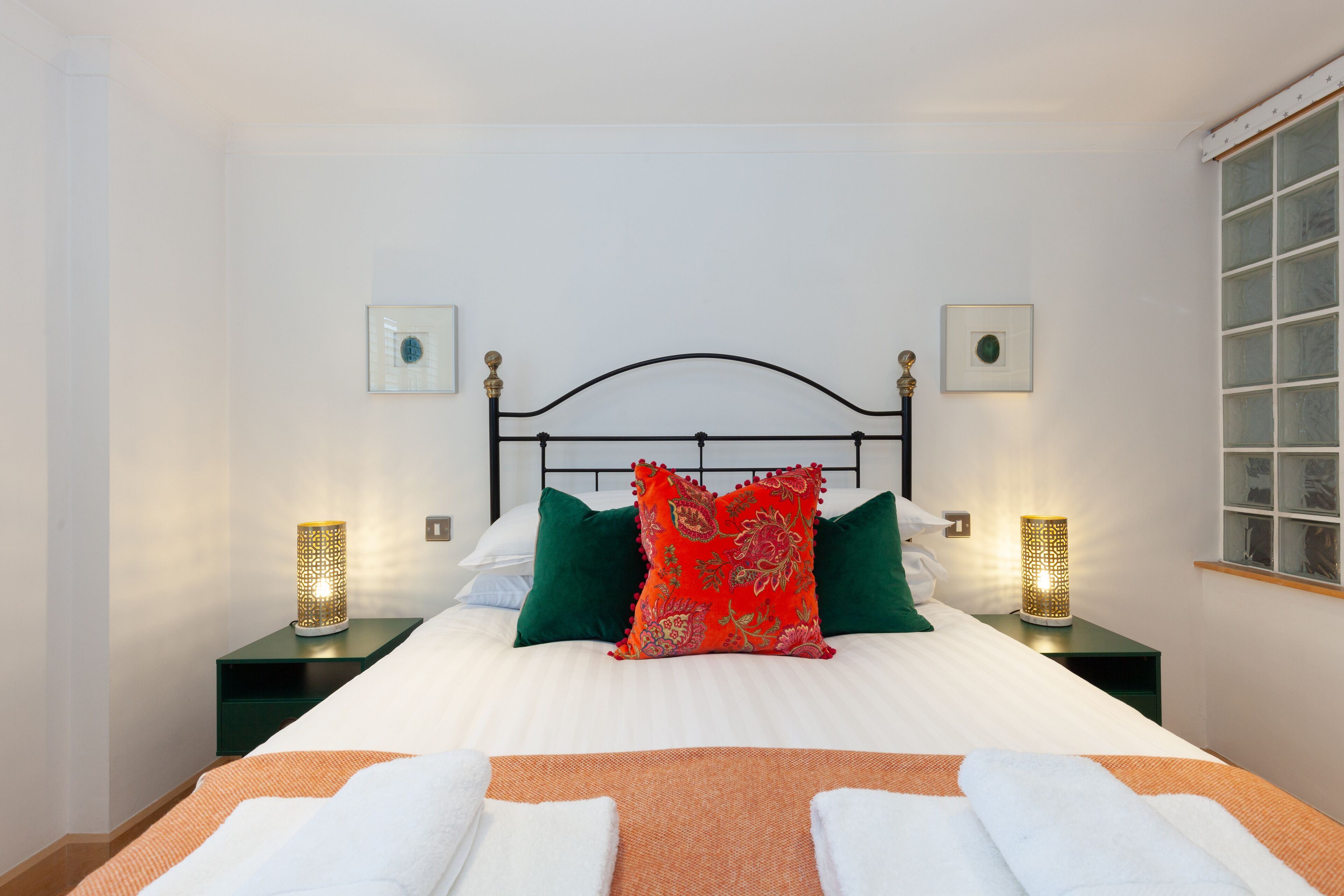 A neatly made bed with a decorative pillow, two bedside tables with lamps, and framed pictures on the walls.
