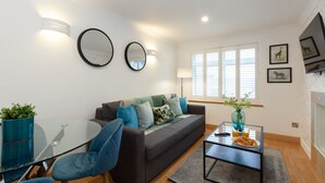 A modern living room with a glass coffee table, a sofa with cushions, a round mirror, and a vase with plants. - Apartment in the hear of the city, live like a local (Oxford)