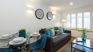 A modern living room with a glass dining table, a sofa, and a coffee table. There are two wall-mounted mirrors and a window with blinds. - Apartment in the hear of the city, live like a local (Oxford)