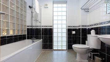 A bathroom with a bathtub, toilet, and sink, featuring black and white tiles and a frosted glass door.
