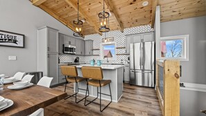 A modern kitchen with grey cabinets, a wooden dining table, and two bar stools. - New Modern Mountain Retreat with Spectacular Views (Sevierville)