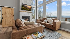 A modern living room with a fireplace, large windows, and a herringbone-patterned wall. - New Modern Mountain Retreat with Spectacular Views (Sevierville)
