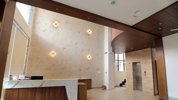 A spacious lobby with a marble reception desk, wooden paneling, and a modern elevator. - Hotel Mumbai House Express (Udaipur)