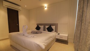 A hotel room with a large bed, a bedside table, a nightstand, and a wall-mounted air conditioner. - Hotel Mumbai House Express (Udaipur)