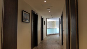 A hallway with patterned flooring, dark wooden doors, and a framed picture on the wall. - Hotel Mumbai House Express (Udaipur)