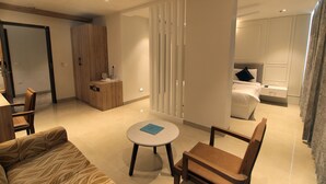 A modern hotel room with a bed, a small sitting area with a table and chairs, a wardrobe, and a bathroom visible through a partition. - Hotel Mumbai House Express (Udaipur)