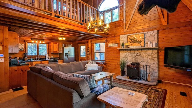 A cozy cabin interior with a wooden dining area, a stone fireplace, and a large TV mounted on the wall. - Smith's Point Retreat on Lake Winnipesaukee with indoor pool! (Alton Bay)