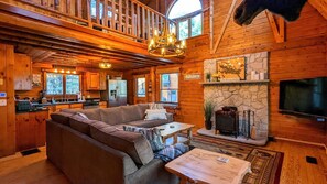 Interior acogedor de una cabaña con comedor de madera, chimenea de piedra y televisor grande montado en la pared.