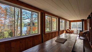 A wooden cabin with large windows, a long dining table, wicker chairs, and a fireplace. - Smith's Point Retreat on Lake Winnipesaukee with indoor pool! (Alton Bay)
