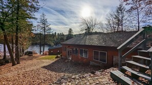 A cabin with a stone foundation, a wooden deck, and a staircase leading to a loft area.