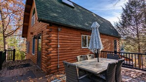 A log cabin with a deck, outdoor table and chairs, and a covered patio area.