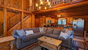 A cozy cabin interior with a wooden staircase, a sectional sofa, a wooden coffee table, and a kitchen area with a refrigerator and microwave. - Smith's Point Retreat on Lake Winnipesaukee with indoor pool! (Alton Bay)