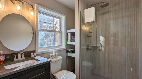 Un baño con un espejo redondo, un lavabo, un inodoro y una zona de ducha con mampara de cristal.