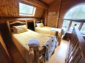 A cabin with two wooden beds, a wooden deck, and a window overlooking a forest.
