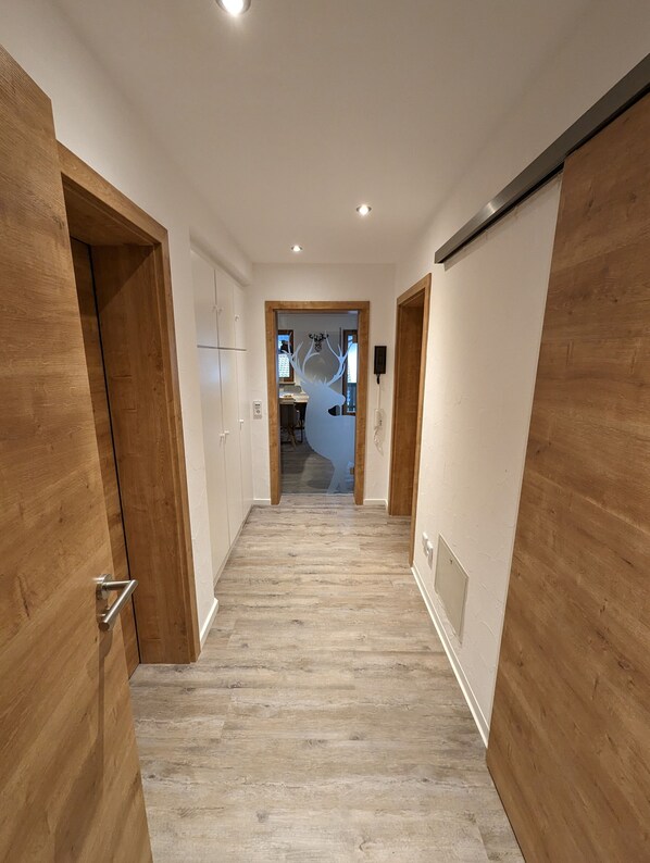 Un pasillo con puertas de madera, paredes blancas y suelo de madera.