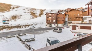 Eine verschneite Straße mit einem Gebäude, das hölzerne Balkone hat, und einem Skilift im Hintergrund.