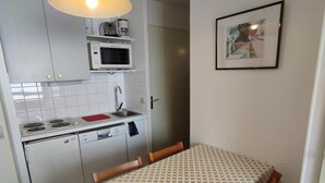 Eine kompakte Küche mit weißen Schränken, einer Mikrowelle, einem Spülbecken und einem Esstisch mit gemustertem Tischläufer.
