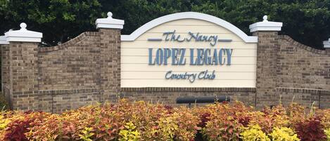Une enseigne indiquant l’entrée du Nancy Lopez Legacy Country Club, avec un mur en briques et des parterres de fleurs aménagés.