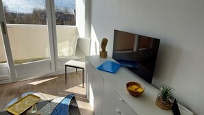 Un salon moderne doté d’un grand téléviseur, de meubles blancs, d’une table basse en verre, d’un tapis à motifs bleus et d’un balcon avec vue.