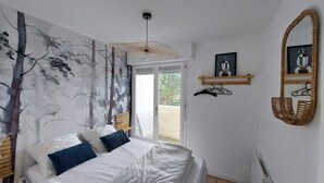 Une chambre avec un lit, une grande fresque murale, un ventilateur de plafond, une porte donnant sur l’extérieur et un miroir sur le mur.