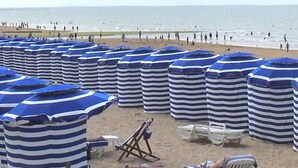 Une plage avec des parasols rayés et des chaises longues blanches.