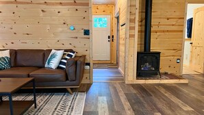 Ein gemütliches Blockhaus-Interieur mit einem braunen Ledersofa, einem gemusterten Teppich, Holzböden, einem Kamin und einer Tür mit Fenster.