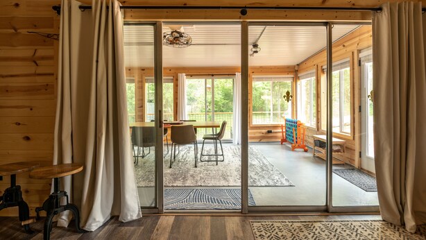 Ein Interieur einer Holzhütte mit Essbereich, eine Schiebetür zu einem Außenbereich mit Tisch und Stühlen.