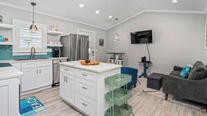 A modern kitchen with white cabinets, a central island, and a dining area with a blue chair.