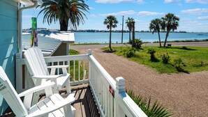 A balcony with white Adirondack chairs overlooking a beach with palm trees and a view of the water.