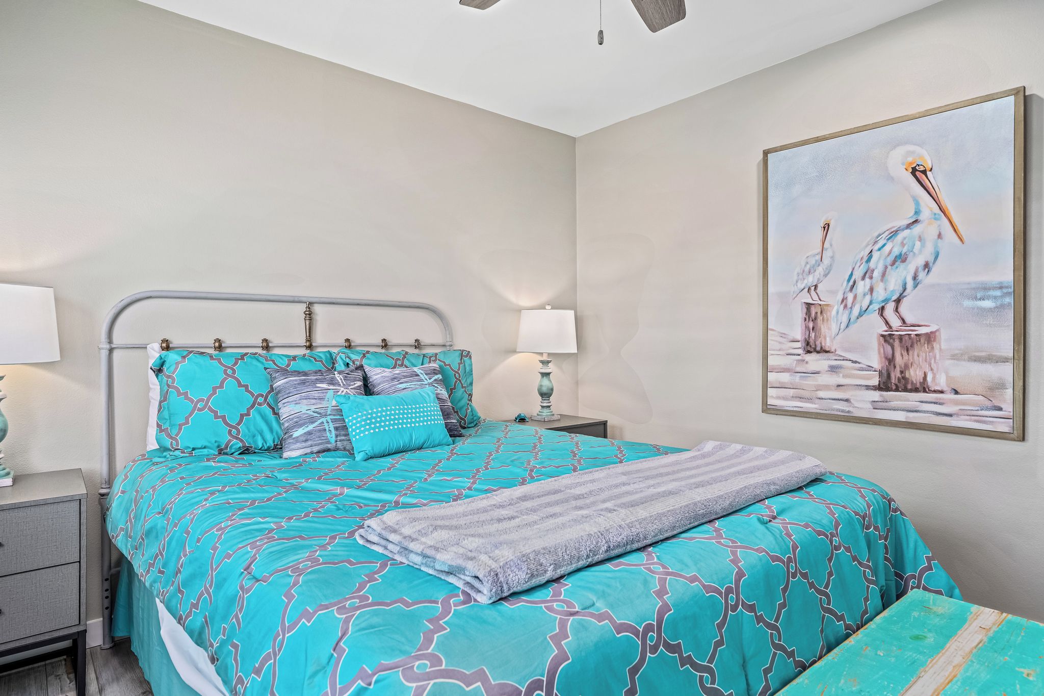 A bedroom with a bed, nightstands, and a painting of pelicans.