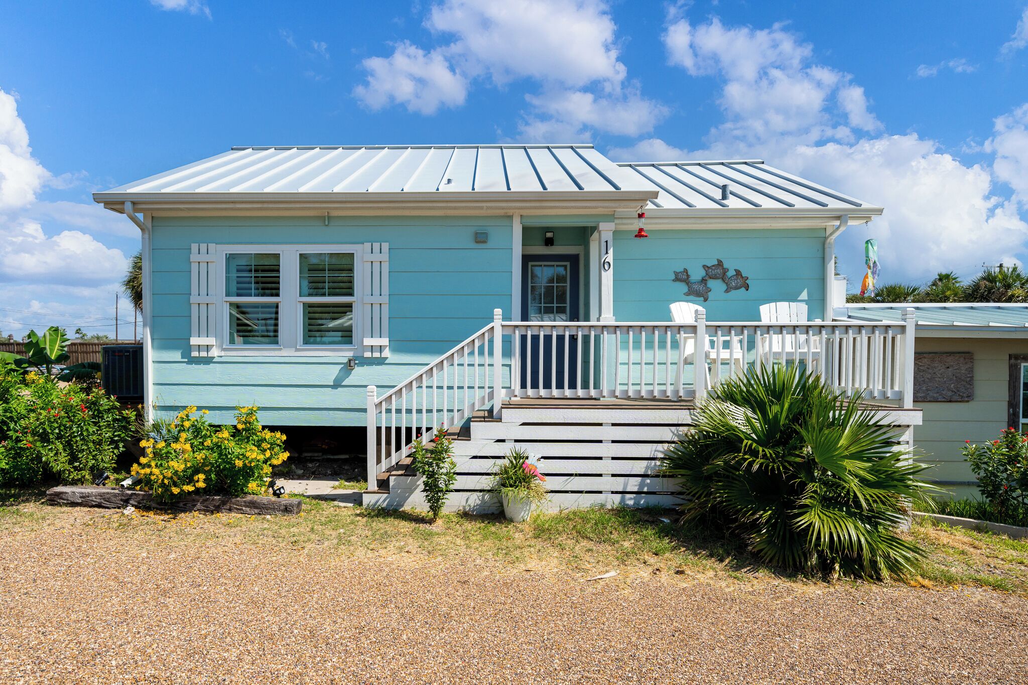 A light blue house with white trim, a front porch with white railings, and a small staircase leading to the door.