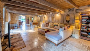A spacious living area with a large sofa, wooden beams, stone flooring, and a bookshelf. - Dezie Manor Grange and Gardens near Sarlat la Caneda (Val de Louyre et Caudeau)