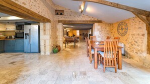 A spacious kitchen with modern appliances, a dining area with wooden furniture, and a stone wall with a clock. - Dezie Manor Grange and Gardens near Sarlat la Caneda (Val de Louyre et Caudeau)