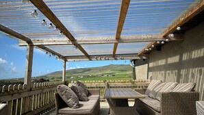 Un patio al aire libre con mobiliario de mimbre, una pérgola y vistas al campo.