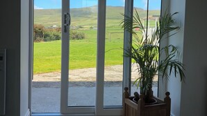 Una habitación con un amplio ventanal corredero que da a un espacio exterior con césped. Hay un banco de madera con una planta en maceta junto a la puerta.